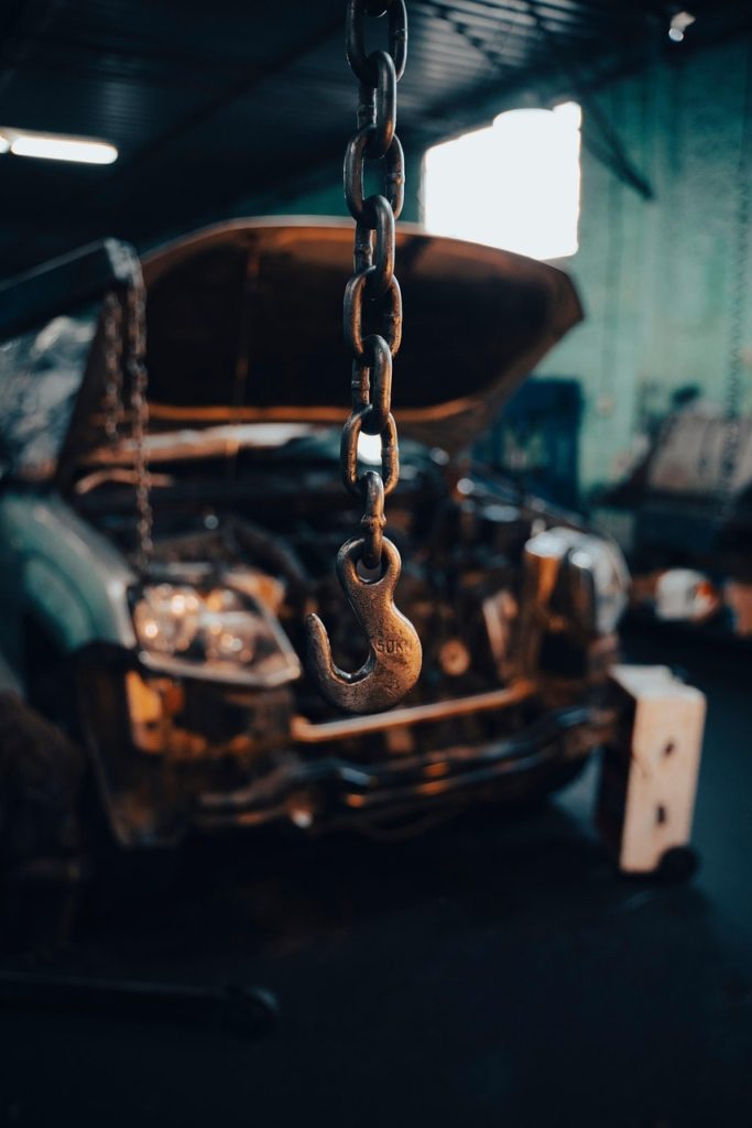 Close-up of industrial hook with damaged car in auto repair garage